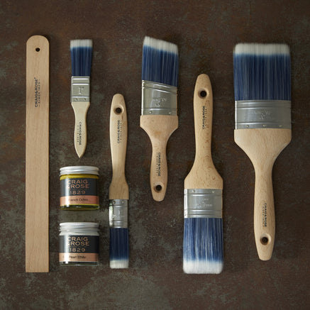 Craig & Rose paint brushes, sample pots of paint and paint stirrer on a Artisan Rust Effect background